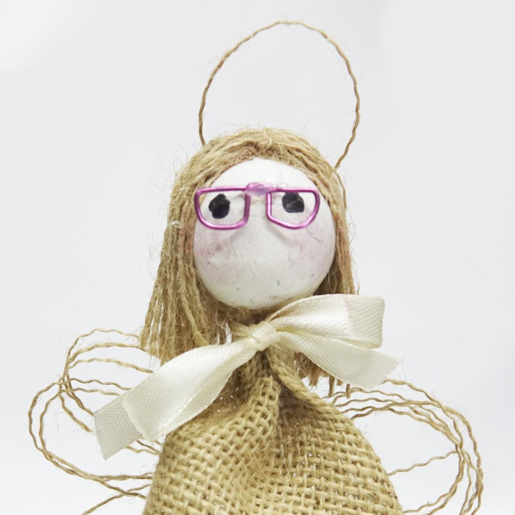 Imagen de Muñeca tipo marioneta de ángel con cabeza de corcho blanco y detalle de gafas y cuerpo de tela de saco con pasamanería y lazo